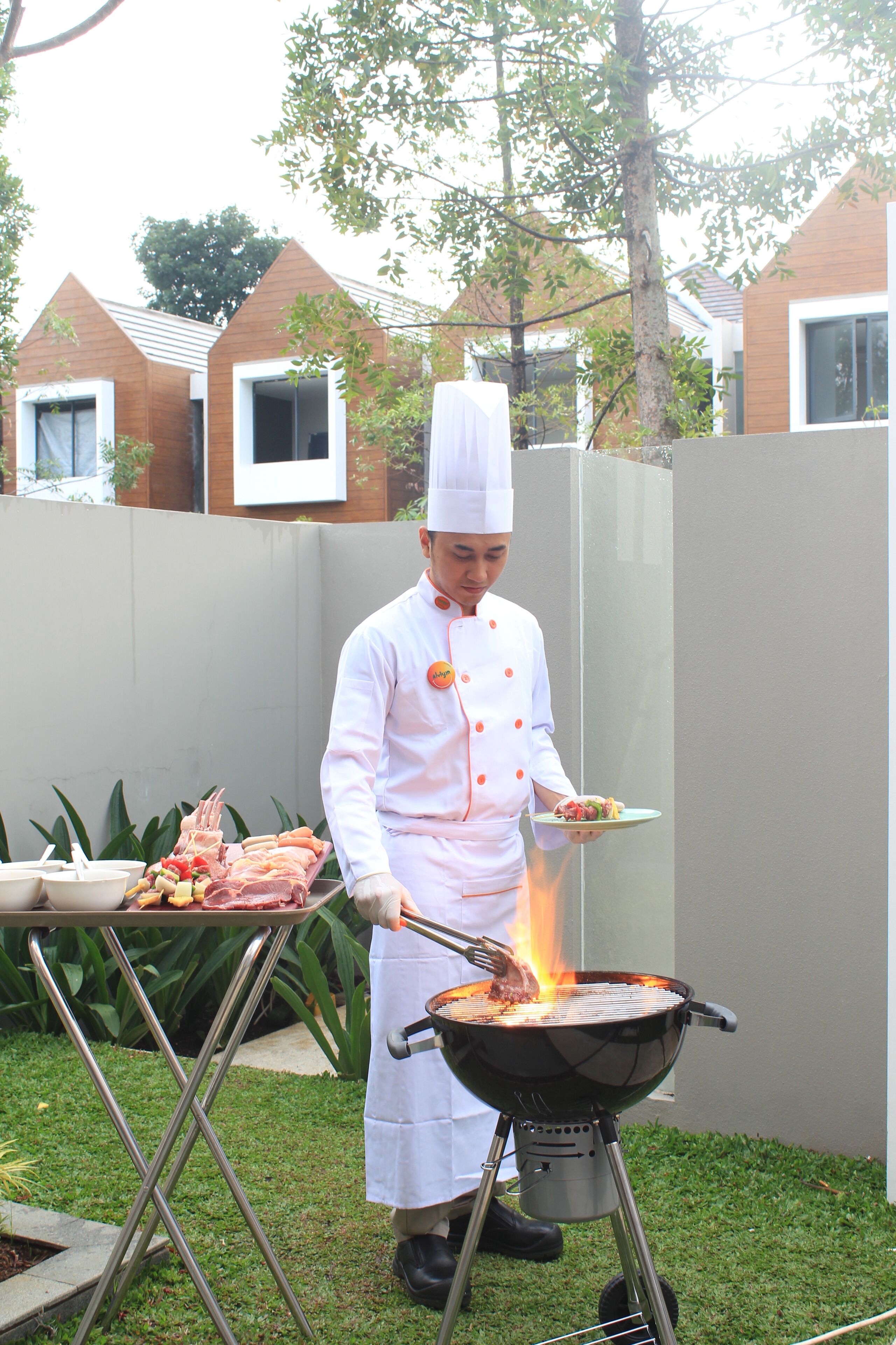 A chef grilling outdoors with a grill and a tray of food.