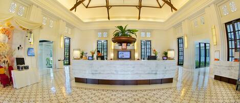 A spacious lobby with a marble reception desk, large windows, and a high ceiling with wooden beams.