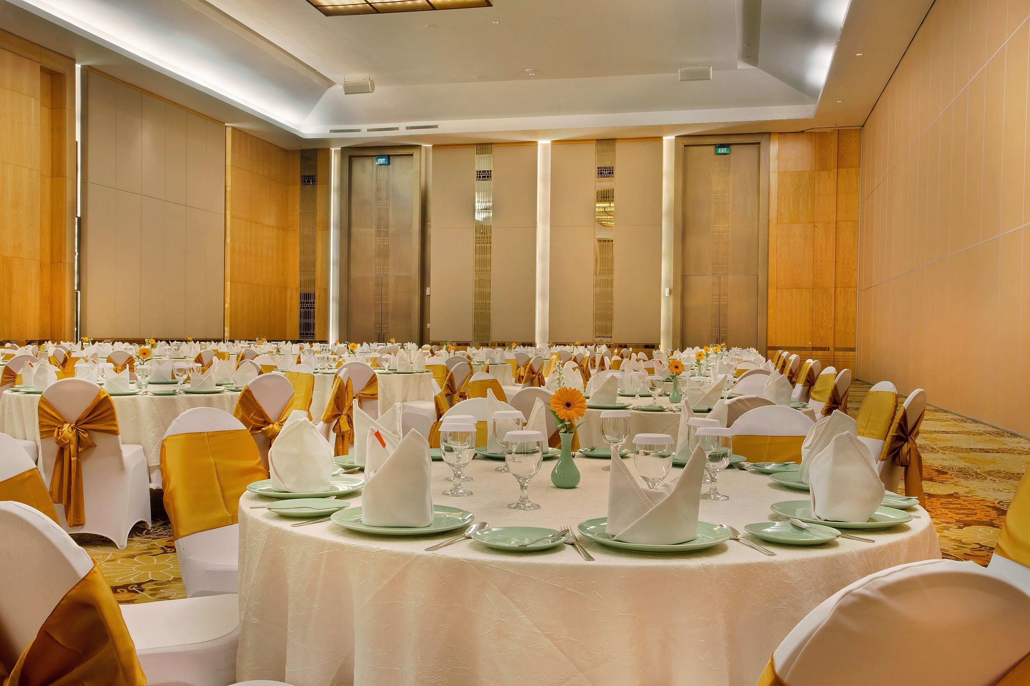 A banquet hall with round tables set for a formal event, featuring white tablecloths, green plates, and gold sashes.