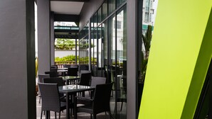 An outdoor patio area with tables and chairs, large windows, and a view of greenery and buildings. - 56 Hotel (Kuching)