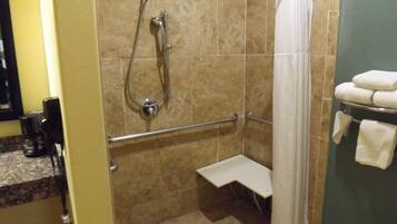 Un espace douche équipé d’un pommeau de douche à main, d’une barre d’appui et d’un porte-serviettes blanc avec des serviettes.