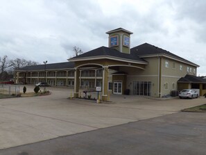 A large hotel with a central entrance, multiple parking spaces, and a covered waiting area. - SUNRISER INN (Kilgore)