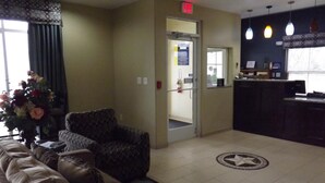 A lobby with a reception desk, a patterned armchair, a sofa, and a decorative vase with flowers. - SUNRISER INN (Kilgore)