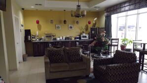 A living room with a sofa, armchairs, and a coffee table. There is a kitchen area with a microwave and a sink. The room has a large window with a view of the outside. - SUNRISER INN (Kilgore)