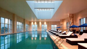 An indoor swimming pool with lounge chairs and umbrellas, large windows, and a skylight. - Four Points By Sheraton Luohe (Luohe)