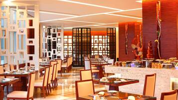A modern restaurant with multiple dining tables and chairs, a central bar area, and a variety of decorative elements.