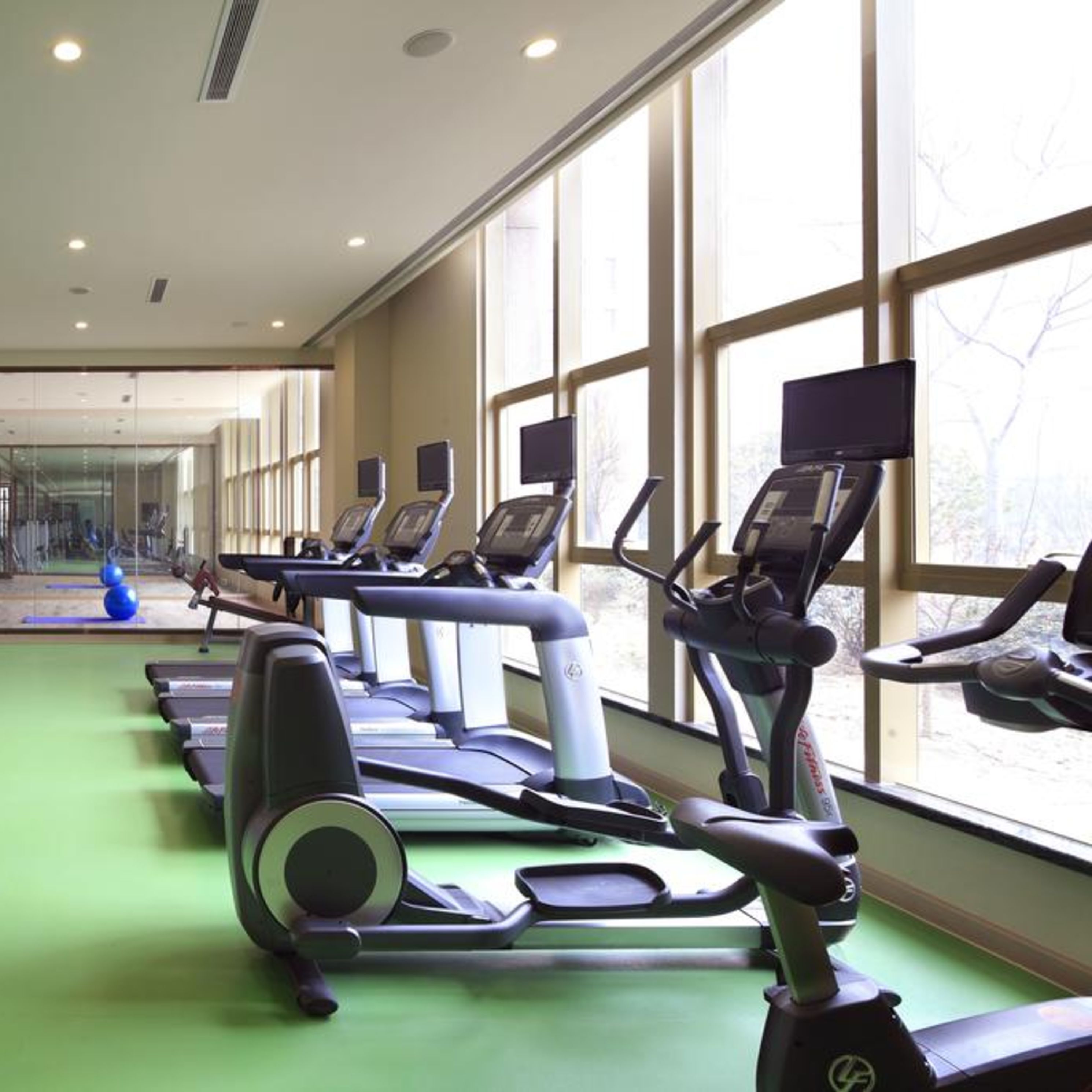 A gym with treadmills and exercise equipment, large windows, and a green floor.