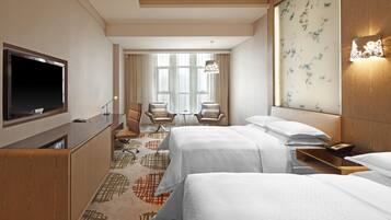 Habitación de hotel con dos camas, televisión, escritorio y zona de estar con sillas.