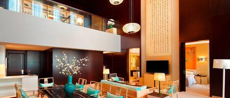 Eine großzügige Hotelhalle mit hoher Decke, einem zentralen Essbereich mit Holzmöbeln und einem großen Fernsehbildschirm.