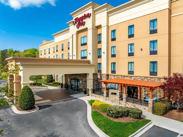 A Hampton Inn hotel with a modern beige facade, multiple windows, and a covered outdoor seating area.