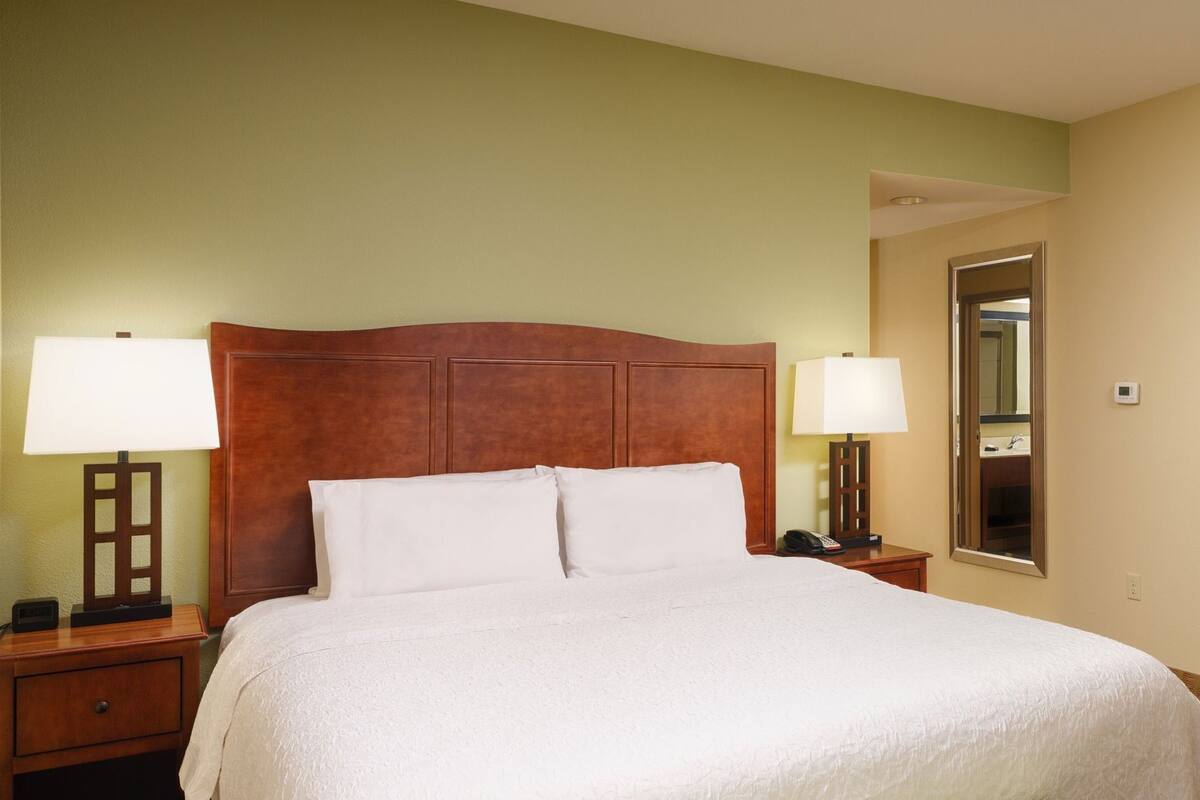 A hotel room with a large bed, two bedside tables with lamps, a nightstand with a phone, and a mirror.