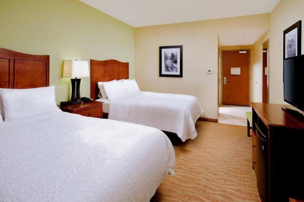 A hotel room with two beds, a TV, a desk, and a door leading to another room.