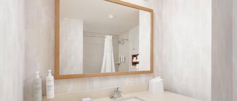 Un baño con un espejo grande, un lavamanos y zona de ducha.