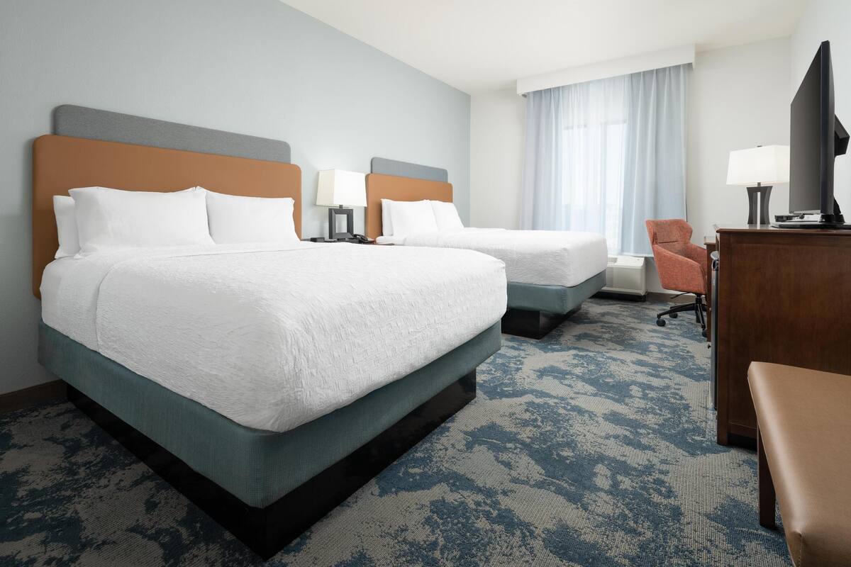 A hotel room with two beds, a desk, a chair, and a television.
