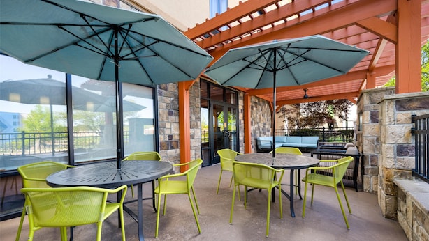 An outdoor patio area with round tables and chairs, covered by umbrellas, and stone walls. - Hampton Inn Cleveland, TN (Cleveland)