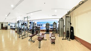 Une salle de sport spacieuse, équipée de divers appareils d’exercice, notamment des bancs et des machines de musculation, et dotée d’un grand mur entièrement recouvert de miroirs.