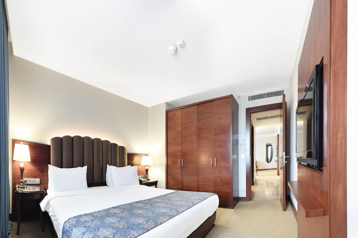 A hotel room with a large bed, a wardrobe, a television, and a desk with a lamp.