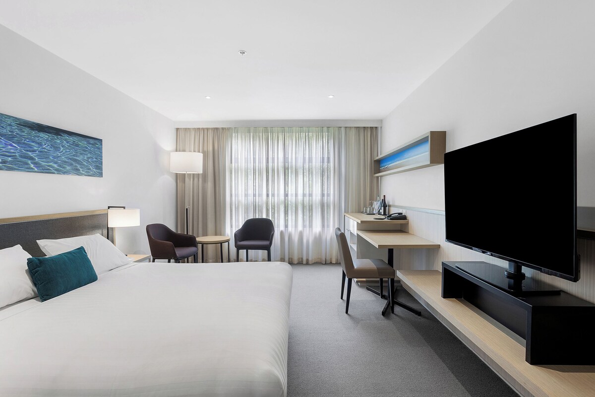 A hotel room with a large bed, a desk, a chair, a television, and a window with curtains.