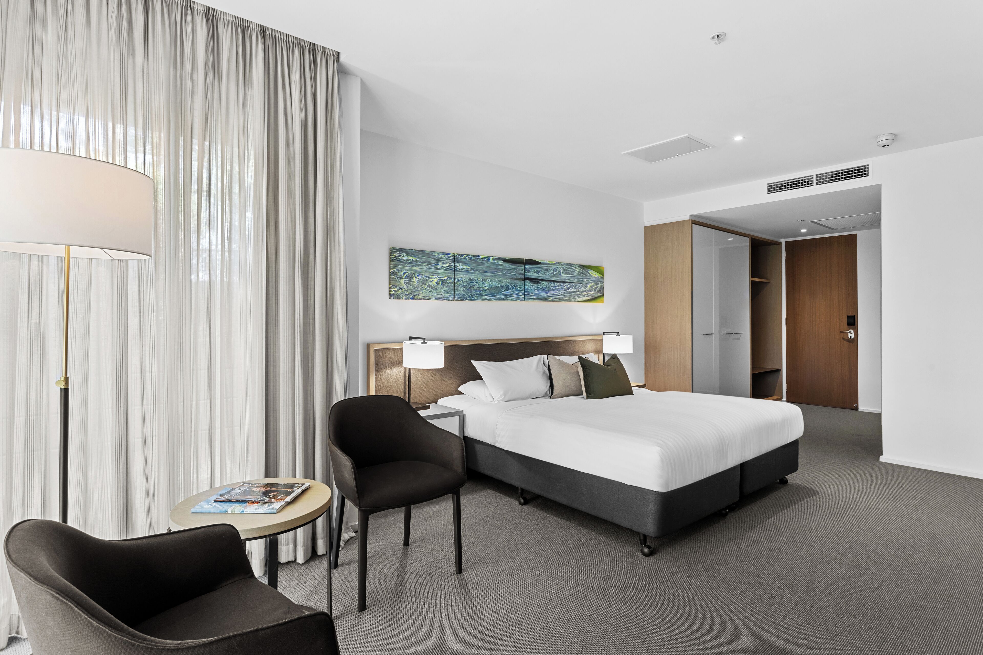 Una habitación de hotel moderna con una cama grande, un escritorio, una silla y un cuadro en la pared.