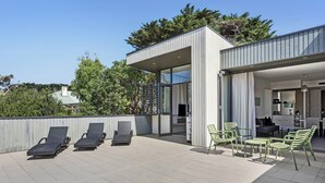 Une terrasse extérieure moderne, dotée de chaises longues et d’un espace repas.