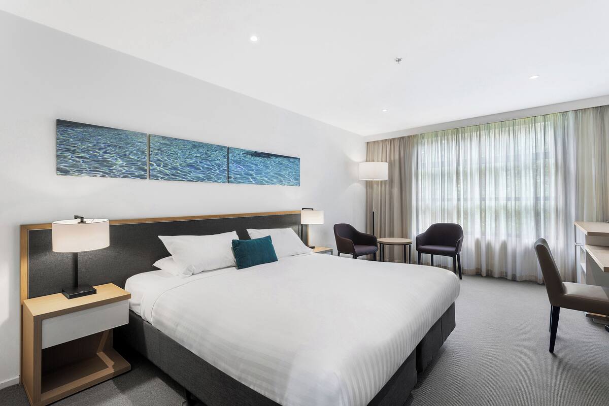 Une chambre d’hôtel avec un grand lit, deux tables de chevet, un bureau, une chaise et une vue sur l’extérieur par la fenêtre.