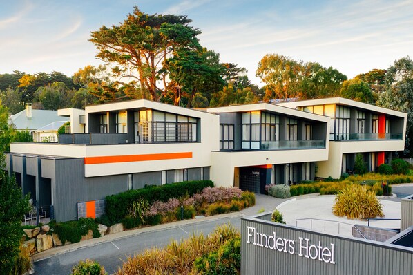A modern hotel with a flat roof, large windows, and a well-maintained garden.