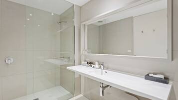 Un baño moderno con ducha acristalada, lavabo blanco y un espejo grande.