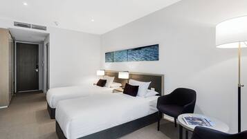 Quarto de hotel com duas camas, uma mesinha, uma cadeira e uma obra de arte na parede.
