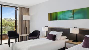 A hotel room with a large bed, two bedside tables, a chair, and a view of greenery through the window.