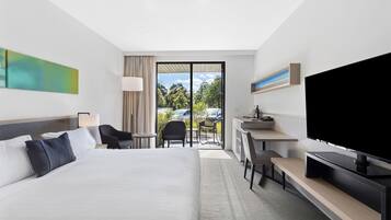 A modern hotel room with a large bed, a desk, a flat-screen TV, and a view of the outdoors.