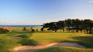 Un parcours de golf avec un drapeau, des bunkers de sable et une vue sur l’océan.