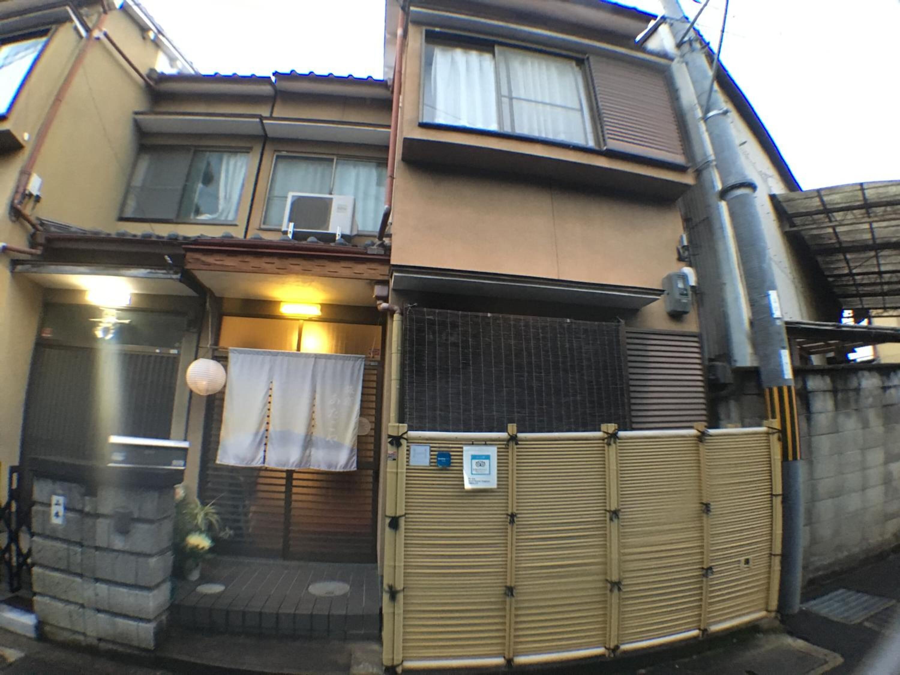 A two-story residential building with a closed gate, a small entrance with a step, and a potted plant.