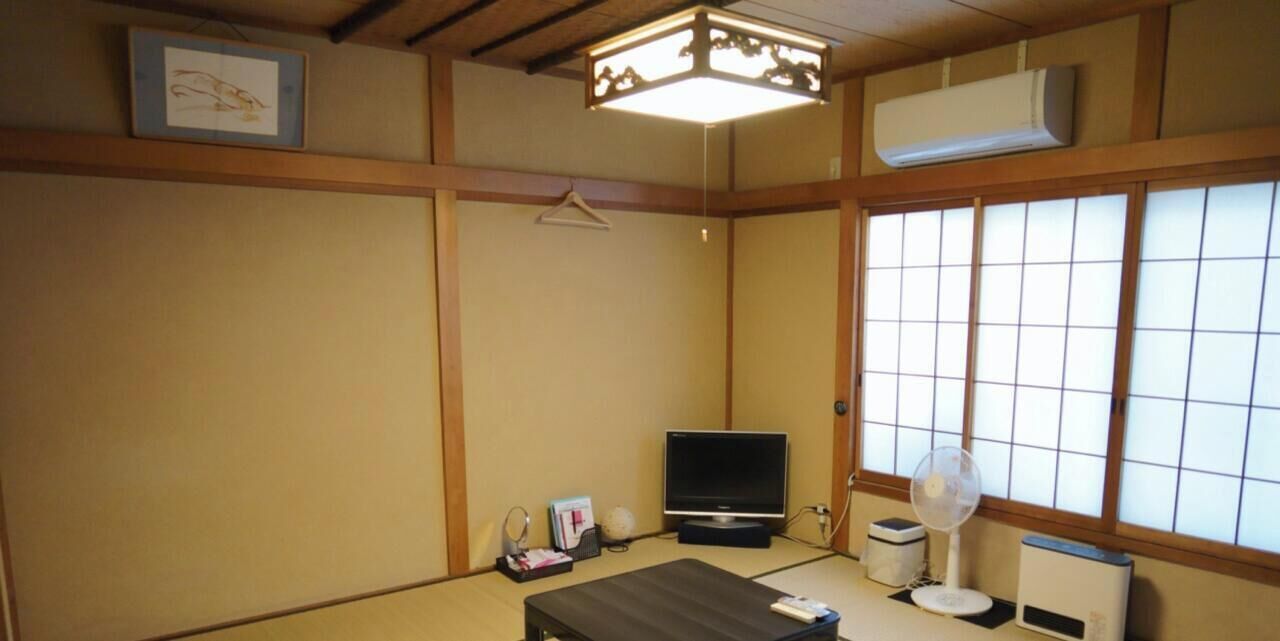 Una habitación japonesa tradicional con suelo de tatami, televisor, ventilador y puertas correderas shoji.