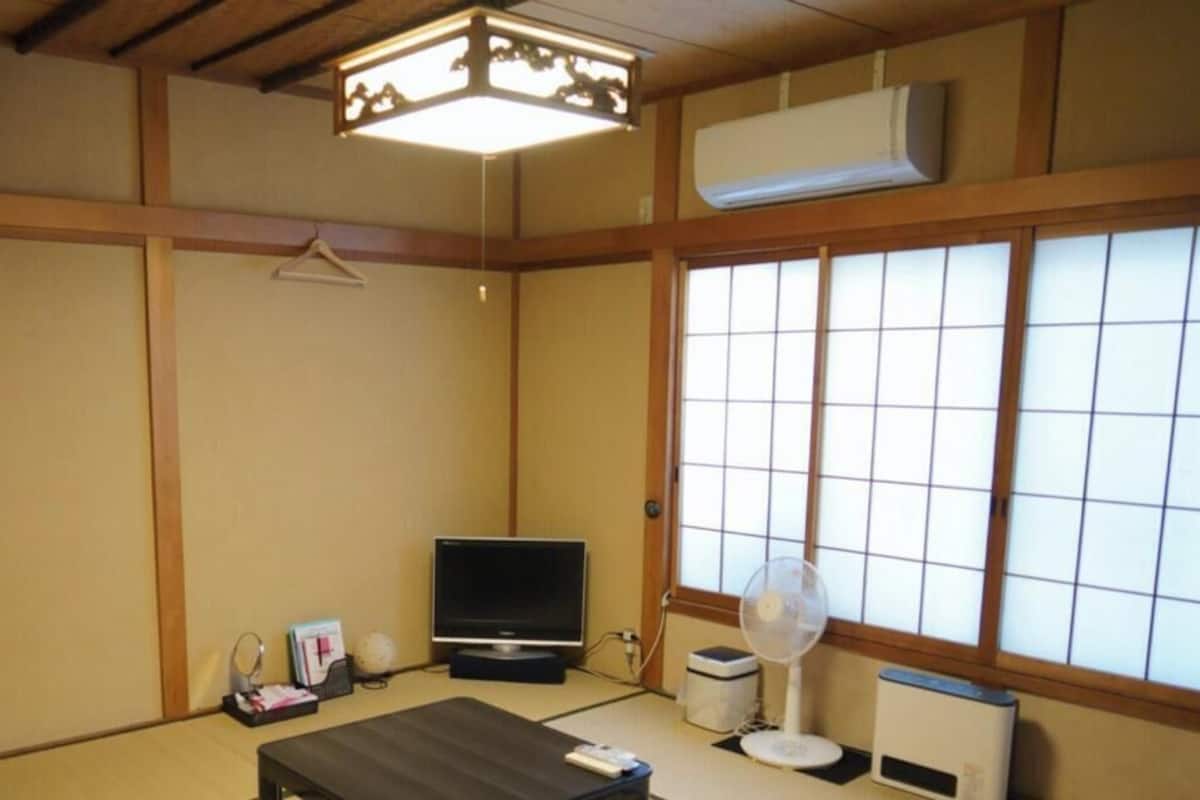 Quarto japonês tradicional com tatames, televisão, ventoinha e um biombó shoji.