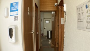 A narrow hallway with wooden doors, a trash bin, and a QR code on the wall.