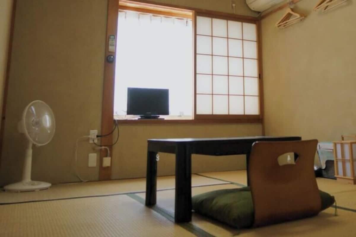 A traditional Japanese room with tatami flooring, a low table, a green cushion, a fan, and a sliding door.