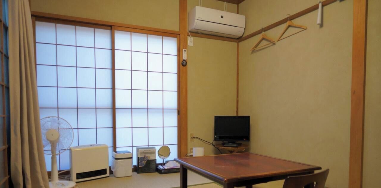 Et traditionelt japansk rum med tatamimåtter, en skydedør i shoji-stil, et fjernsyn, en ventilator og et bord.