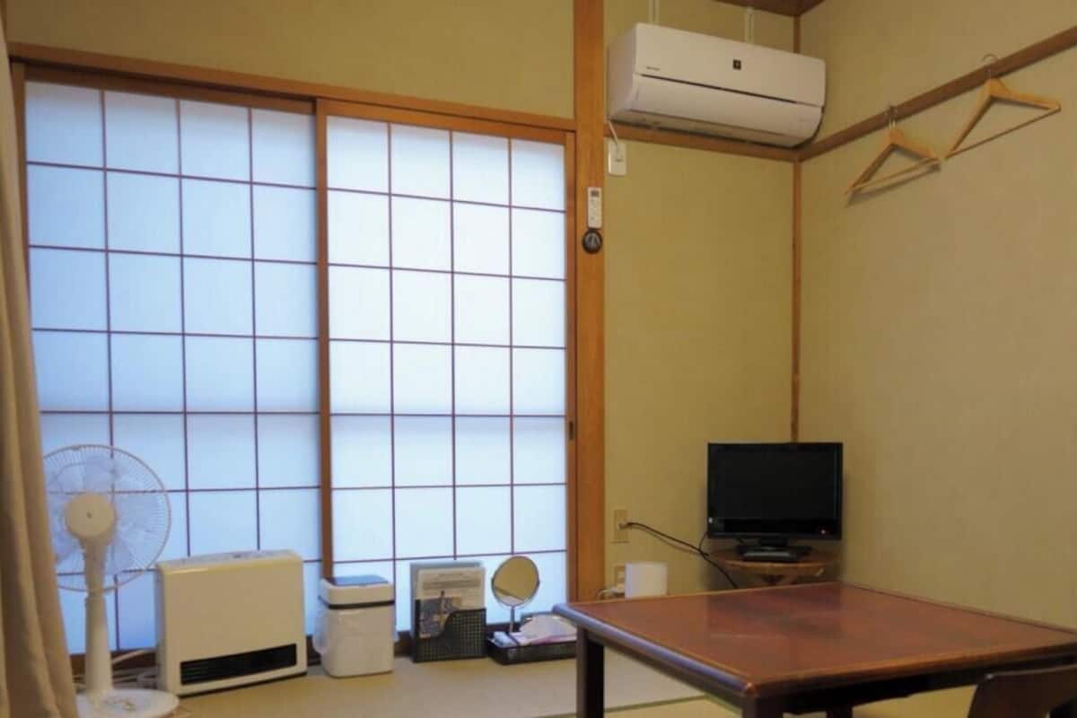 A traditional Japanese room with tatami flooring, a sliding shoji screen door, a television, a fan, and a table.
