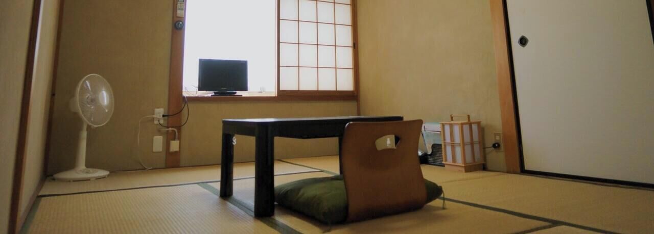 Una habitación con tatami, una mesa baja, un abanico y una pantalla tradicional japonesa.