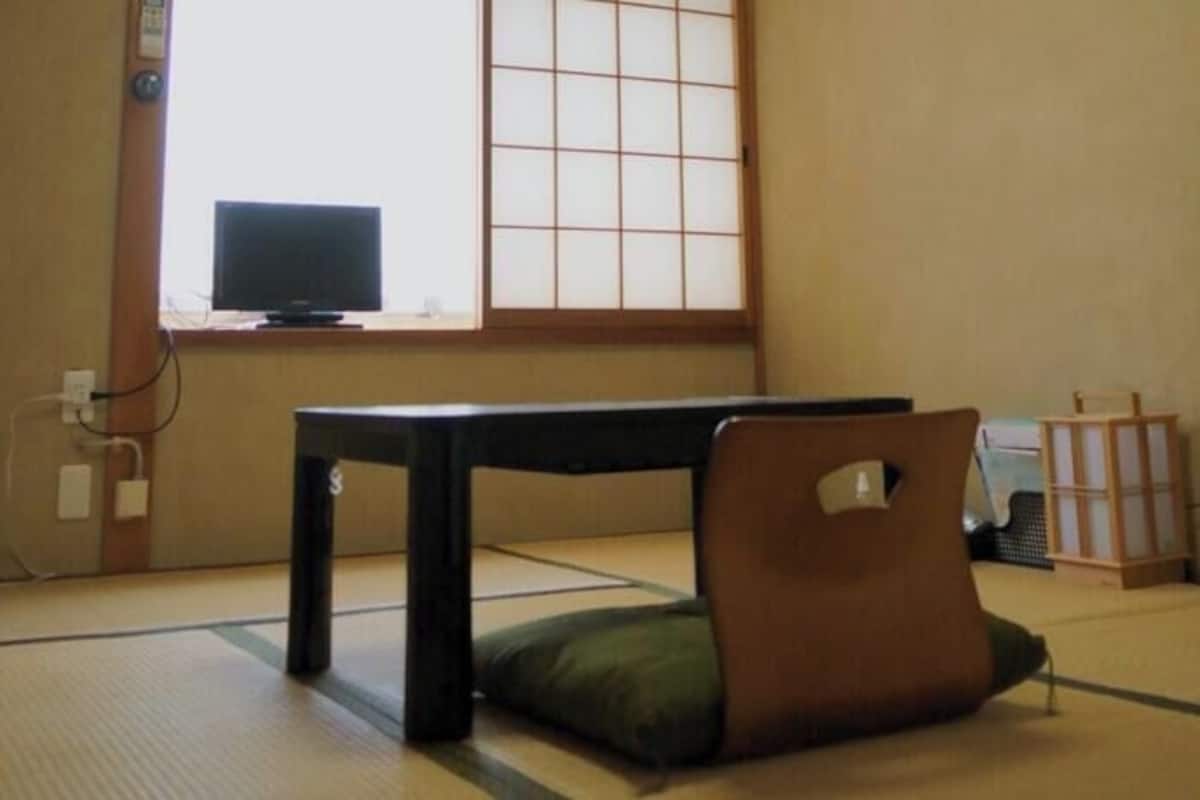 Um espaço com tatames, uma mesa baixa, um leque e um painel decorativo tradicional japonês.