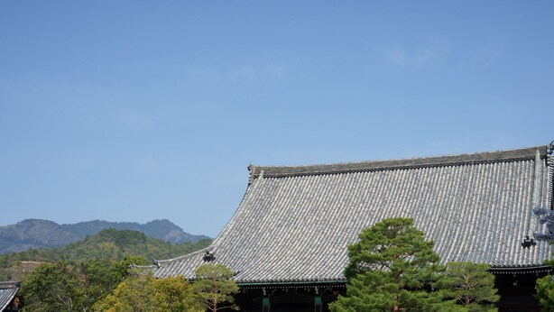 A traditional Japanese building with a tiled roof, surrounded by greenery and mountains in the background.