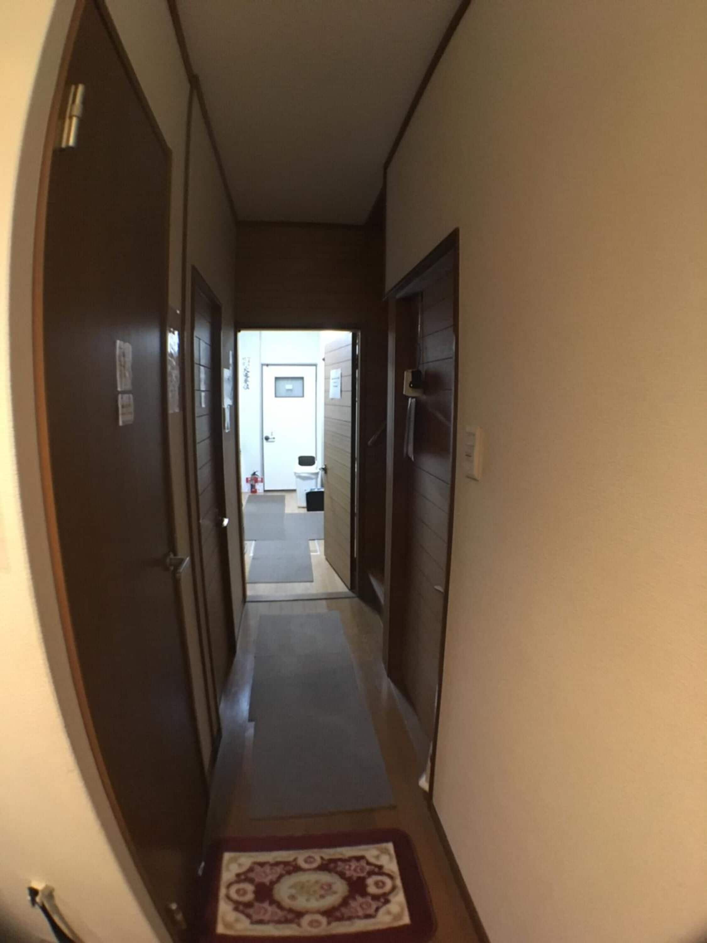A narrow hallway with doors on both sides leading to a room with a white sink and a small window.