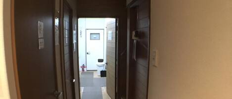 A narrow hallway with doors on both sides leading to a room with a white sink and a small window.