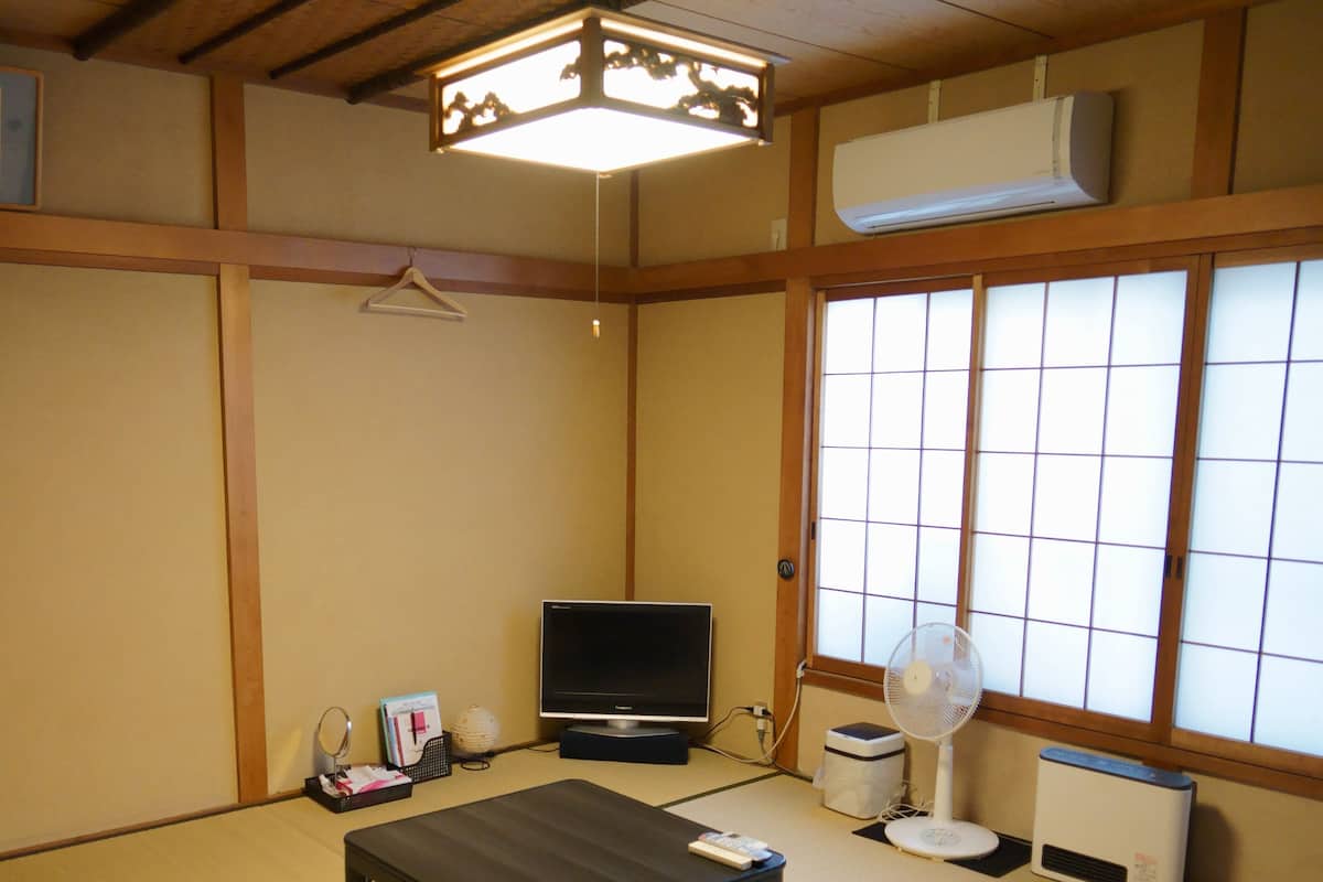 Quarto japonês tradicional com tatames, televisão, ventoinha e aquecedor.