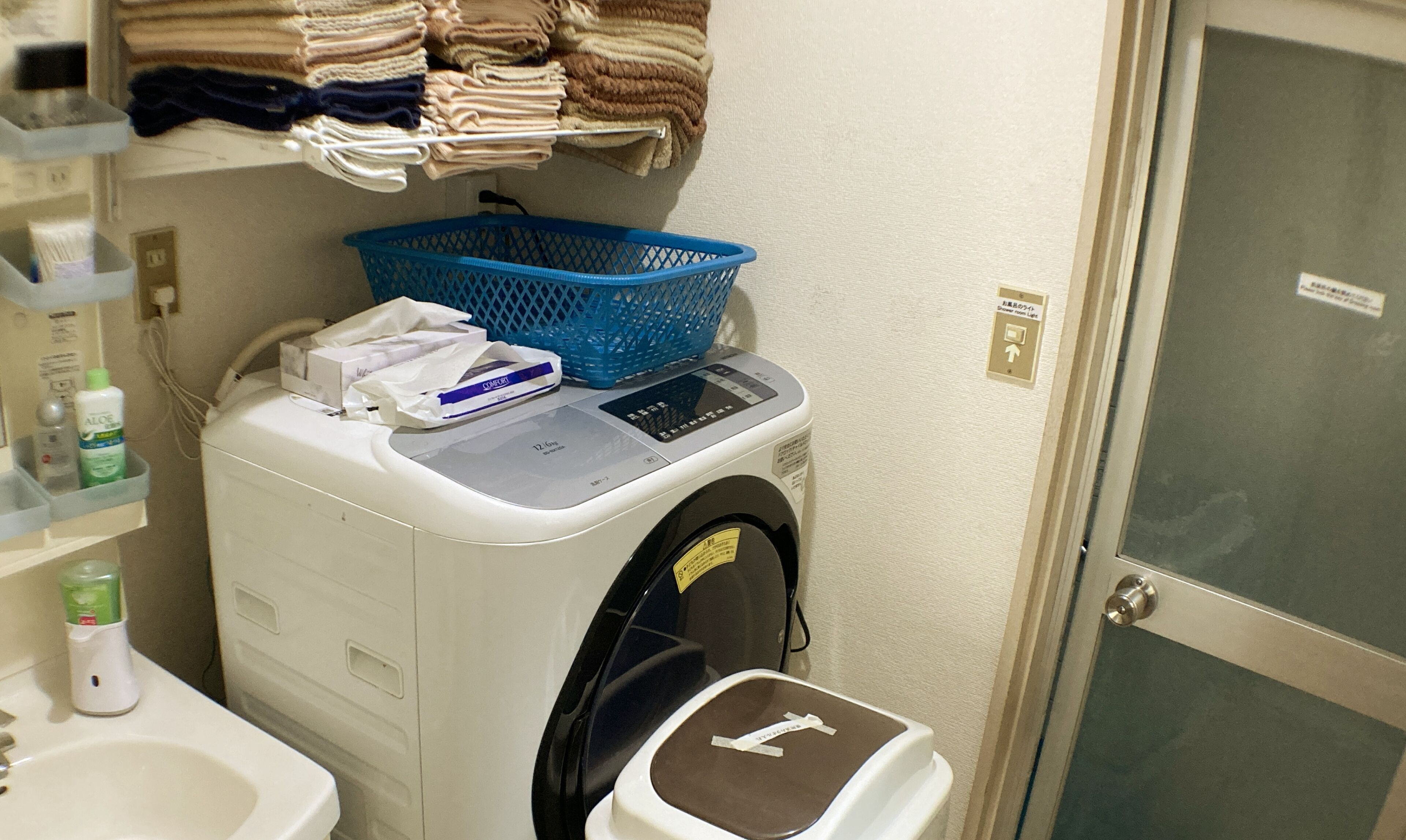 A laundry machine with a control panel, a blue laundry basket, and a towel rack above it.
