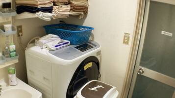 A laundry machine with a control panel, a blue laundry basket, and a towel rack above it.
