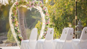 A wedding arch with floral decorations, white chairs, and a statue in the background. - Grand Sea Beach Resort (Ko Pha-ngan)