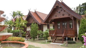 A traditional wooden house with a tiled roof, surrounded by a garden with a fountain and palm trees. - Grand Sea Beach Resort (Ko Pha-ngan)