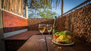 A wooden table with two wine glasses and a bottle of wine, accompanied by a plate of fruit and nuts. - Etosha Village (Okaukuejo)