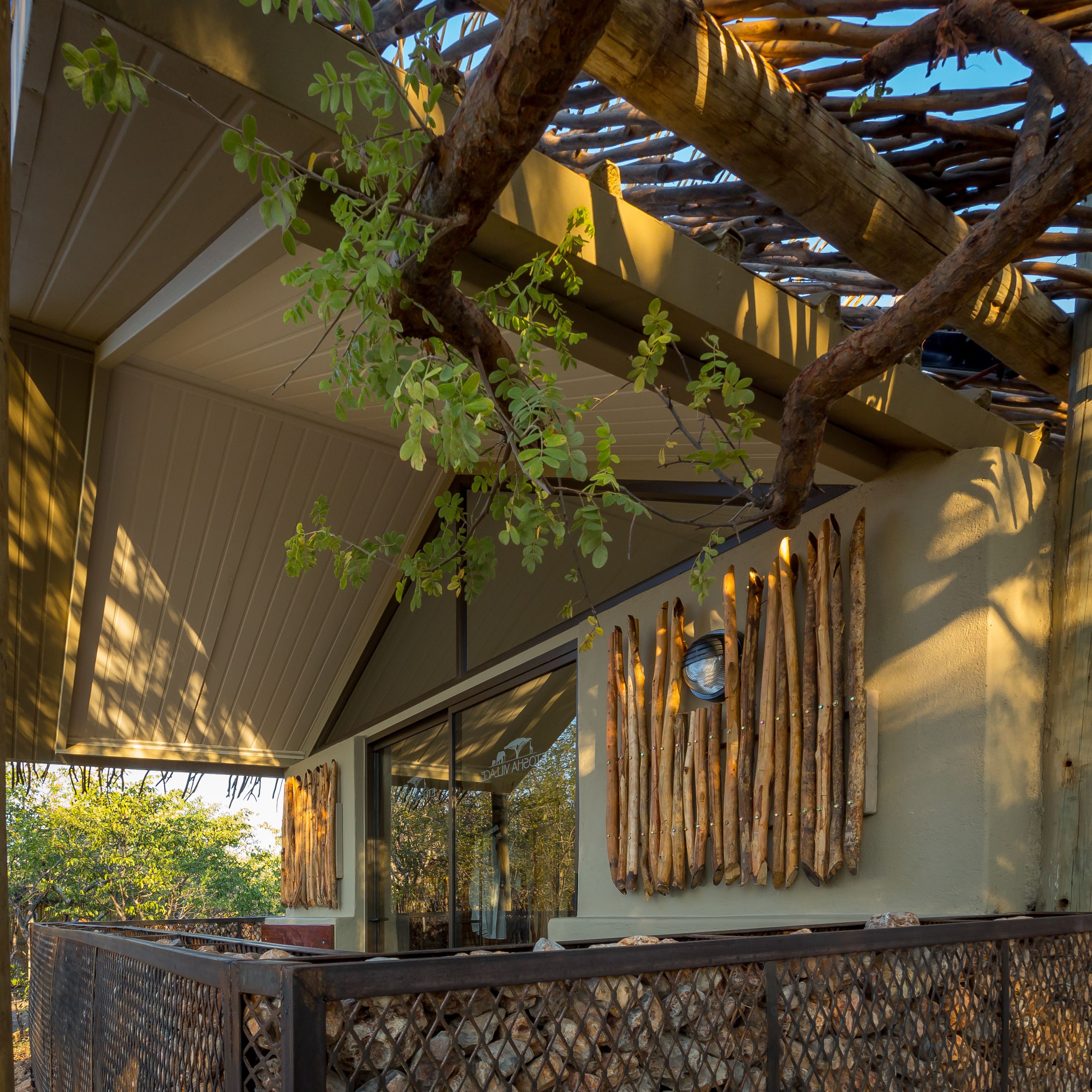 A covered outdoor area with a pergola, a wall with wooden slats, and a view of trees.